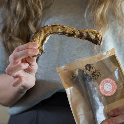 Two air-dried duck neck dog chews on a rustic surface, natural dental snack for dogs.