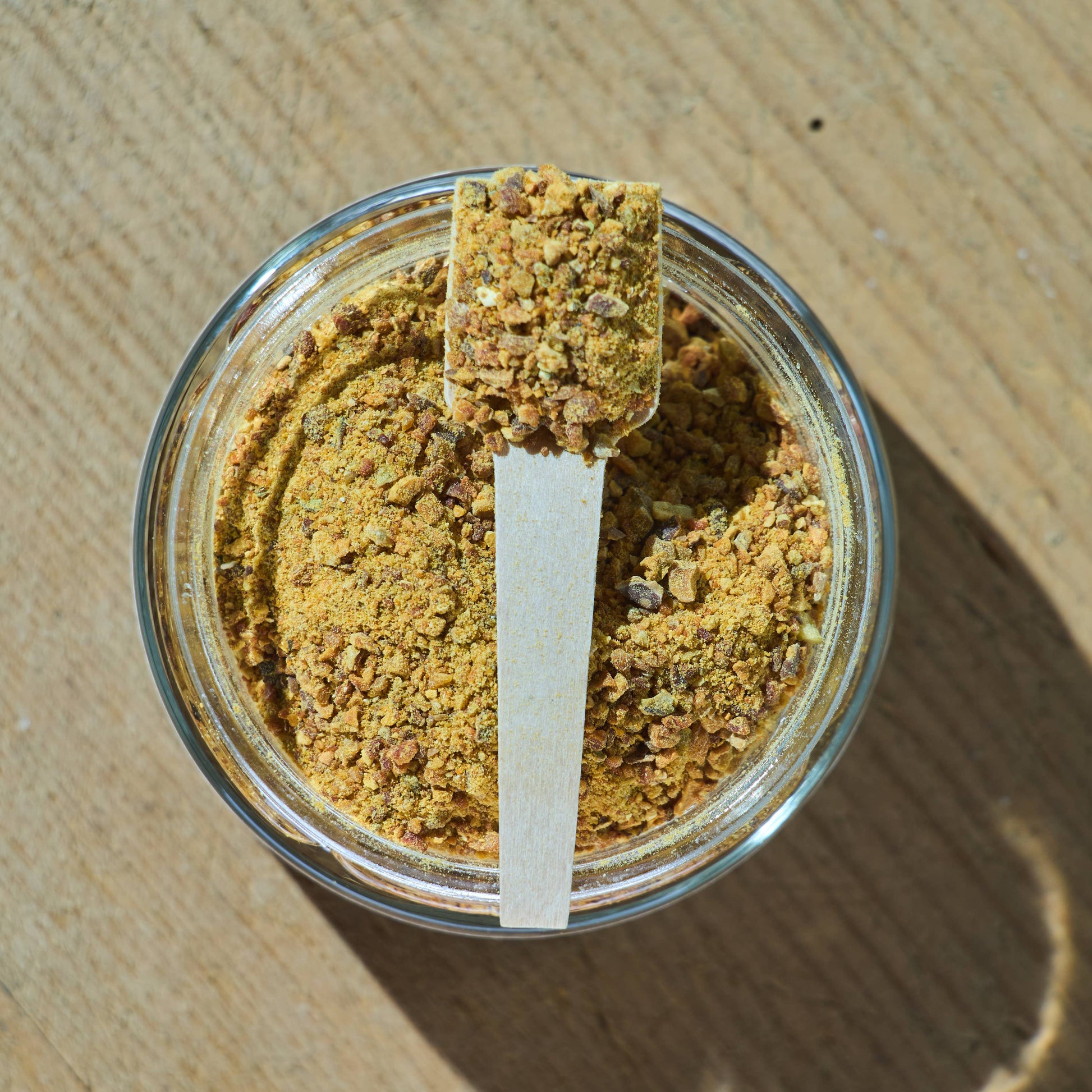 Glass jar of natural dehydrated pumpkin topper for dogs and cats with a wooden spoon, digestive health supplement.
